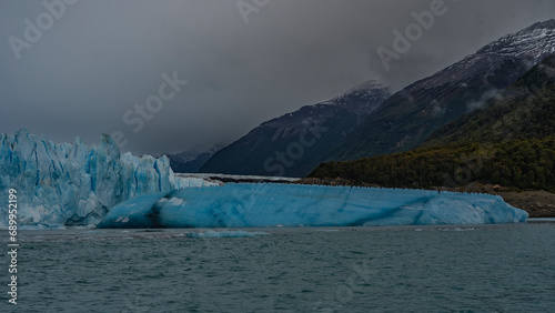 An amazing glacier in a turquoise glacial lake. A wall of blue cracked ice against a cloudy sky and mountain slopes. Argentina. El Calafate. Perito Moreno. Los Glaciares National Park