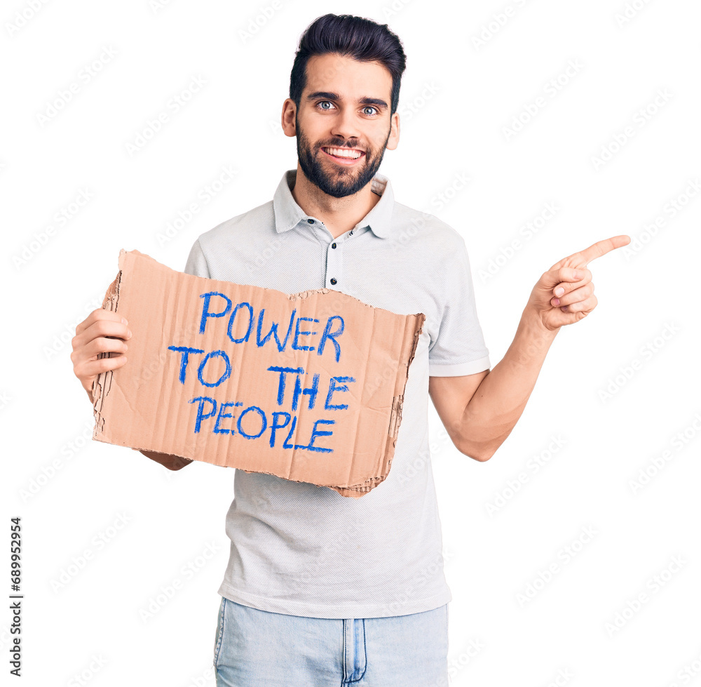 Young handsome man with beard holding power to the people cardboard banner smiling happy pointing with hand and finger to the side Young handsome man with beard holding power to the people cardboard banner smiling happy pointing with hand and finger to the side