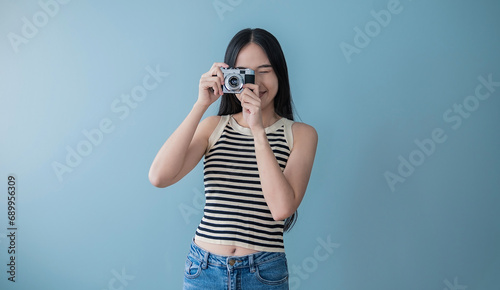 Portrait of beautiful asian woman photographer in fashion look taking photo. Pretty cool young woman model with camera isolated on blue background with copy space banner. Asian travel lady girl. © paulaphoto