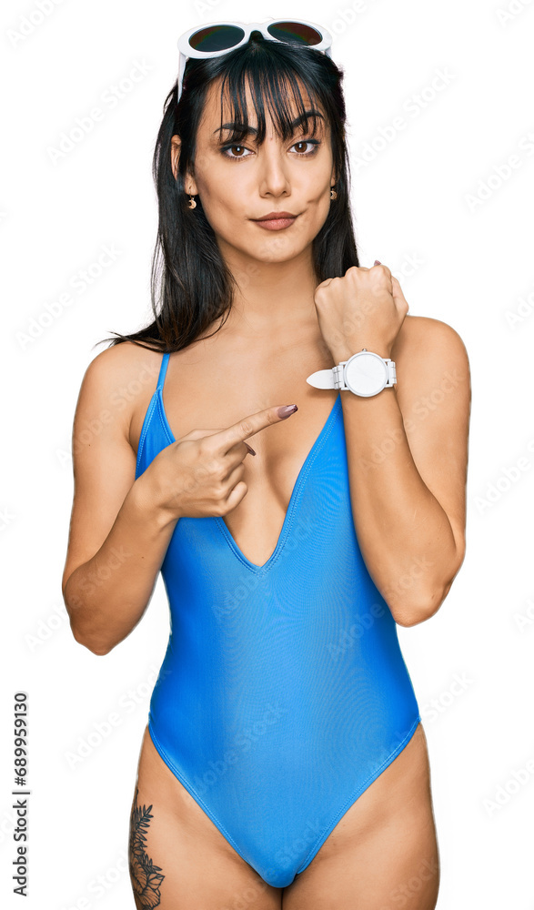 Young hispanic woman wearing swimsuit and sunglasses in hurry pointing to watch time, impatience, looking at the camera with relaxed expression Young hispanic woman wearing swimsuit and sunglasses in hurry pointing to watch time, impatience, looking at the camera with relaxed expression
