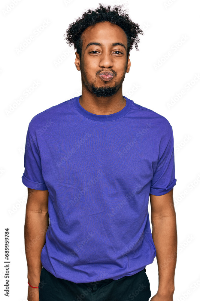 Young african american man with beard wearing casual purple t shirt puffing cheeks with funny face. mouth inflated with air, crazy expression. Young african american man with beard wearing casual purple t shirt puffing cheeks with funny face. mouth inflated with air, crazy expression.