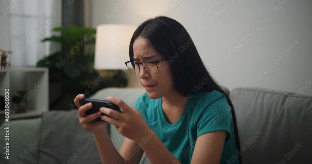 Portrait of Young Asian woman serious playing an online game frustrated with loss or failure sitting on sofa in living room at home,Gamer lifestyle concept. Portrait of Young Asian woman serious playing an online game frustrated with loss or failure sitting on sofa in living room at home,Gamer lifestyle concept.