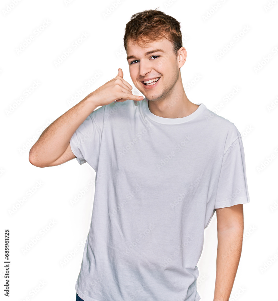 Young caucasian man wearing casual white t shirt smiling doing phone gesture with hand and fingers like talking on the telephone. communicating concepts. Young caucasian man wearing casual white t shirt smiling doing phone gesture with hand and fingers like talking on the telephone. communicating concepts.