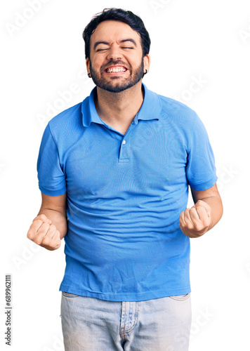 Young hispanic man wearing casual clothes very happy and excited doing winner gesture with arms raised, smiling and screaming for success. celebration concept.