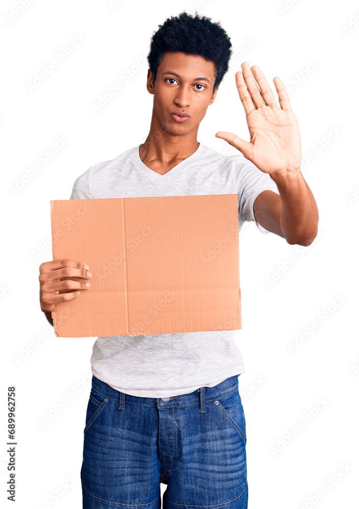 Young african american man holding banner cardboard with open hand doing stop sign with serious and confident expression, defense gesture Young african american man holding banner cardboard with open hand doing stop sign with serious and confident expression, defense gesture