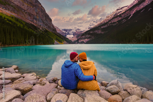 Lake Louise Banff National Park in the Canadian Rocky Mountains. A young couple of men and women sitting on a rock by the lake during a cold day in Autumn in Canada watching the sunset at the lake photo
