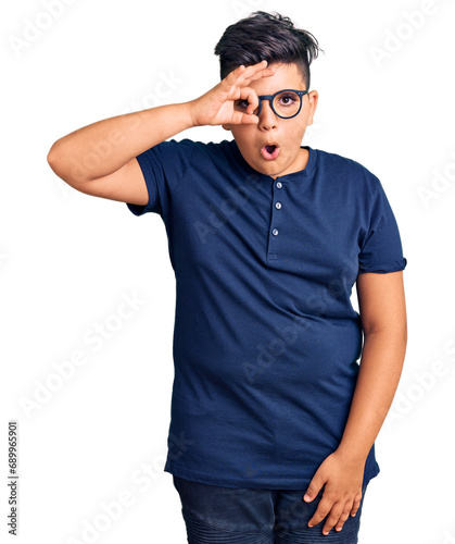 Little boy kid wearing casual clothes and glasses doing ok gesture shocked with surprised face, eye looking through fingers. unbelieving expression.