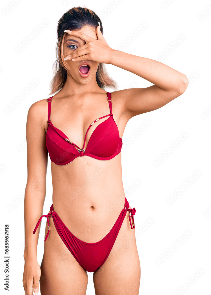 Fototapeta premium Young beautiful woman wearing bikini peeking in shock covering face and eyes with hand, looking through fingers with embarrassed expression.