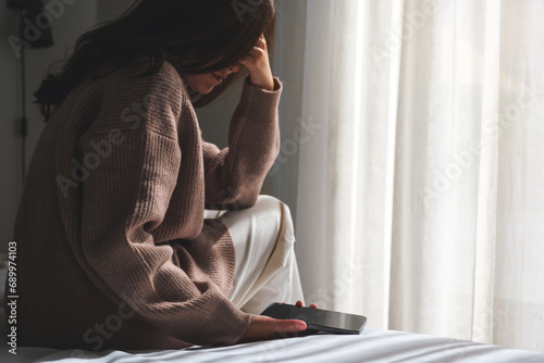 A sad woman after reading bad news on smartphone in bedroom photo