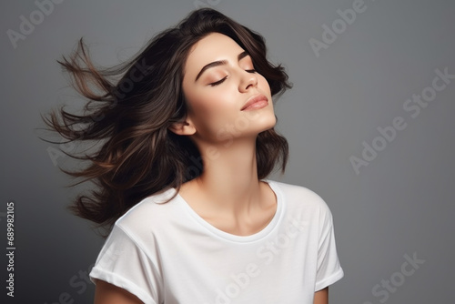 Beautiful young woman wearing a white t-shirt Close your eyes and feel happy and relaxed. Isolated empty space on a gray background.