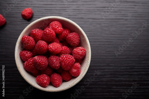 Top view of raspberries in a bowl on wood table background.