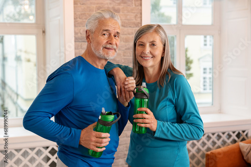 Elderly couple holding bottle of water with smile from thirst after exercise. Happy elderly man and woman smiling. photo