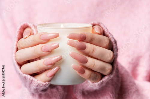 Woman in a pink sweater with a pink manicure holds a candle