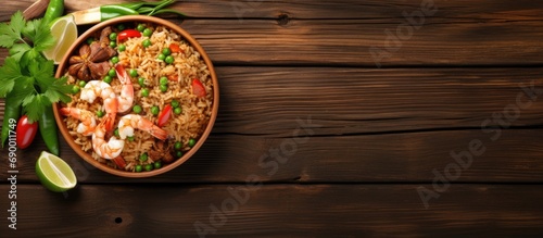 Thai food on a wooden table top view with space for text, featuring classic shrimp fried rice with fresh shrimp, rice, green onions, vegetables, and lime in a bowl.