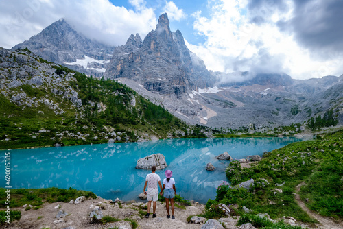 A couple of men and women visit Lago di Sorapis in the Italian Dolomites during summer holidays, milky blue lake Lago di Sorapis or Lake Sorapis Dolomites, Italy.