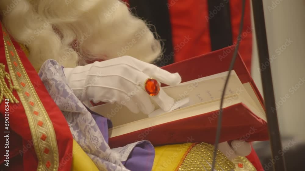 Hand of Saint Nicholas with white glove and ruby ring leafing through holy red book
