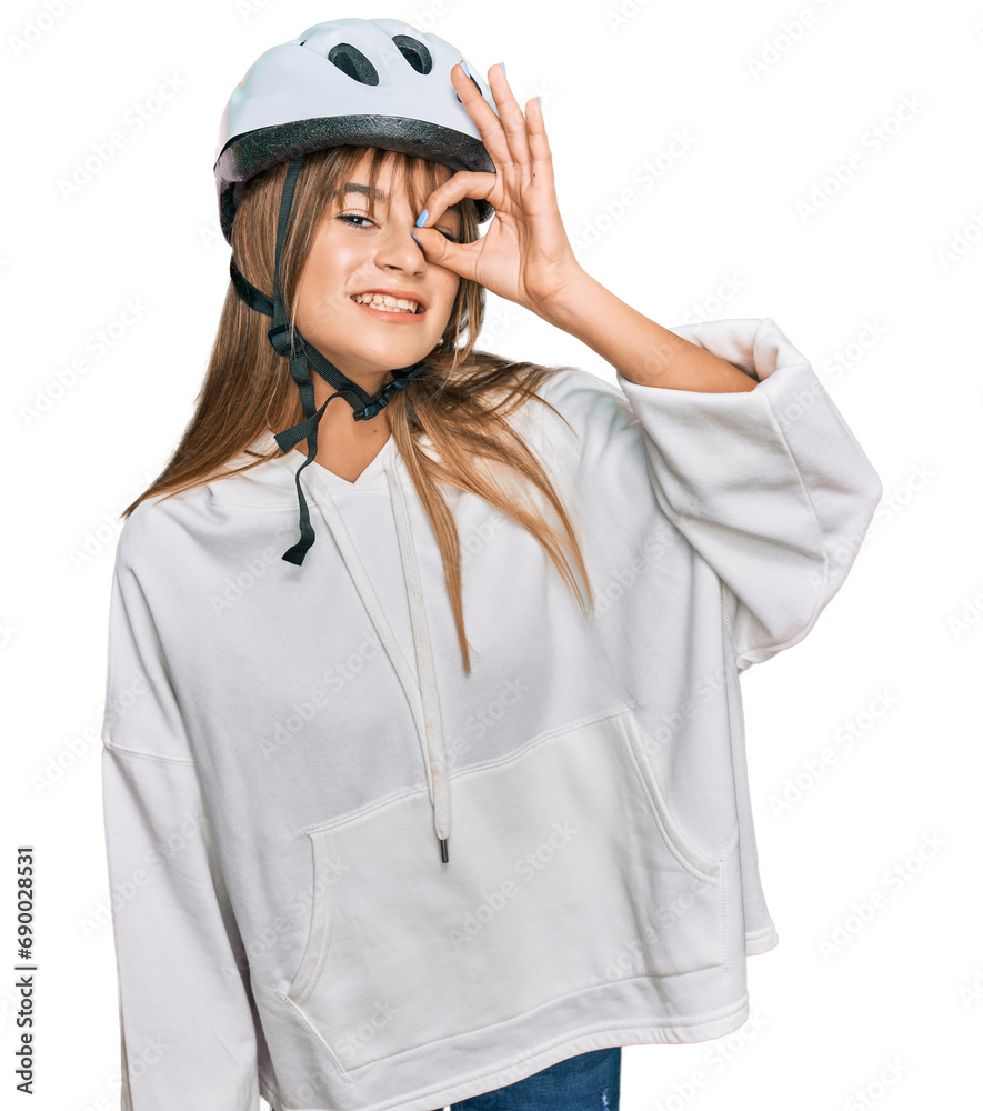 Teenager caucasian girl wearing bike helmet doing ok gesture with hand smiling, eye looking through fingers with happy face. Teenager caucasian girl wearing bike helmet doing ok gesture with hand smiling, eye looking through fingers with happy face.