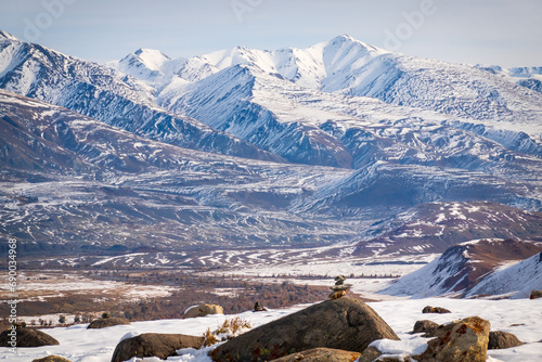 Snowy mountain landscape with rocky foreground and a clear blue sky in Altai