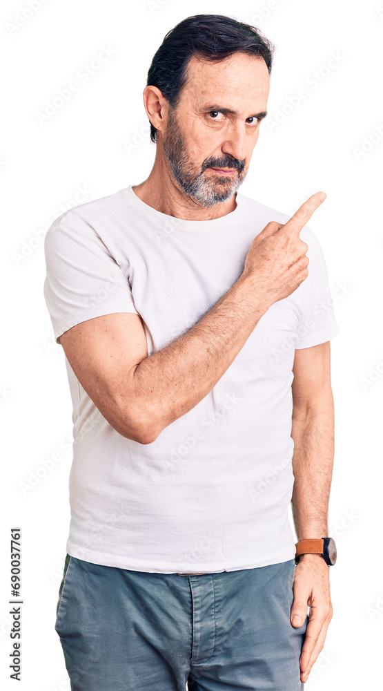 Middle age handsome man wearing casual t-shirt pointing with hand finger to the side showing advertisement, serious and calm face