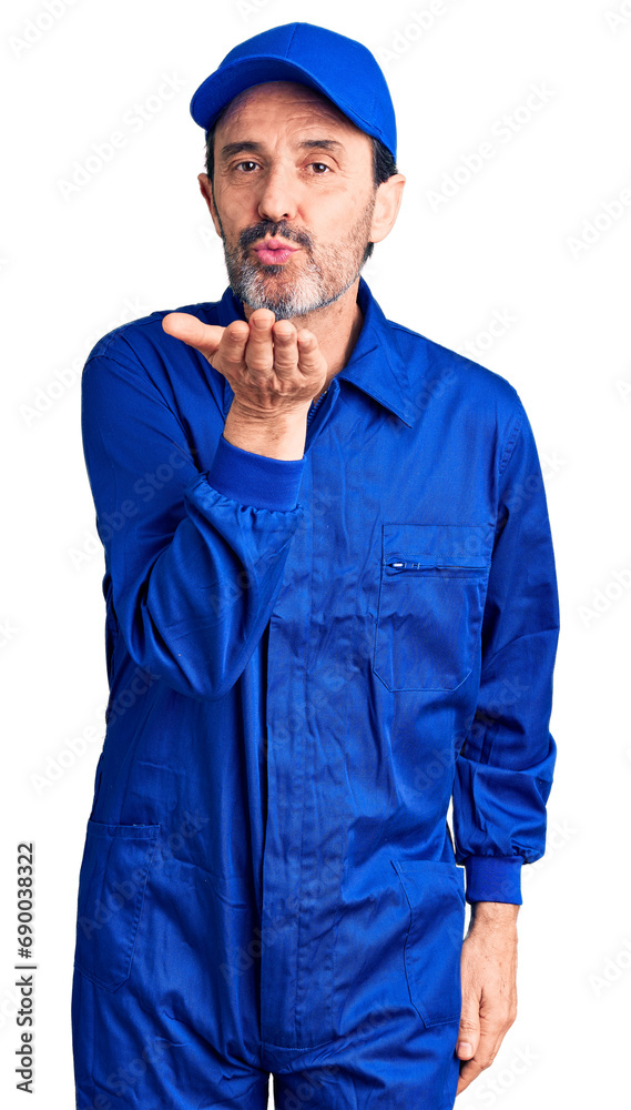 Middle age handsome man wearing mechanic uniform looking at the camera blowing a kiss with hand on air being lovely and sexy. love expression.