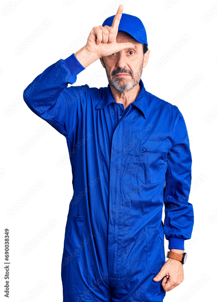 Middle age handsome man wearing mechanic uniform making fun of people with fingers on forehead doing loser gesture mocking and insulting.