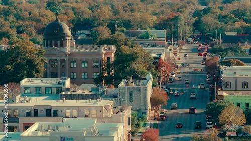 Main Street in downtown Georgetown, Texas during golden hour on fall day, city council building and cars, telephoto aerial drone sweep