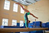 Wide shot of female gymnast doing handstand split on balance beam in gym, copy space