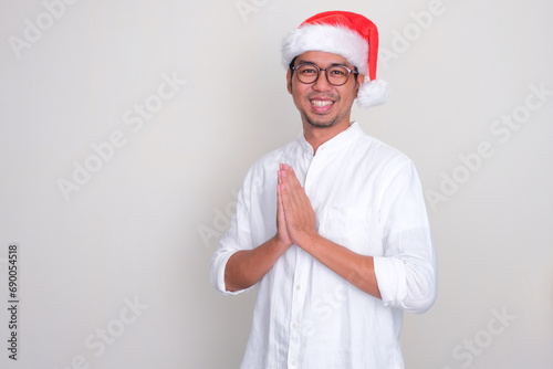 A man wearing christmas hat doing greeting gesture with happy expression photo