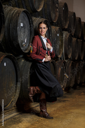 Happy young woman venenciador standing with venencia and with foot on wine barrel photo