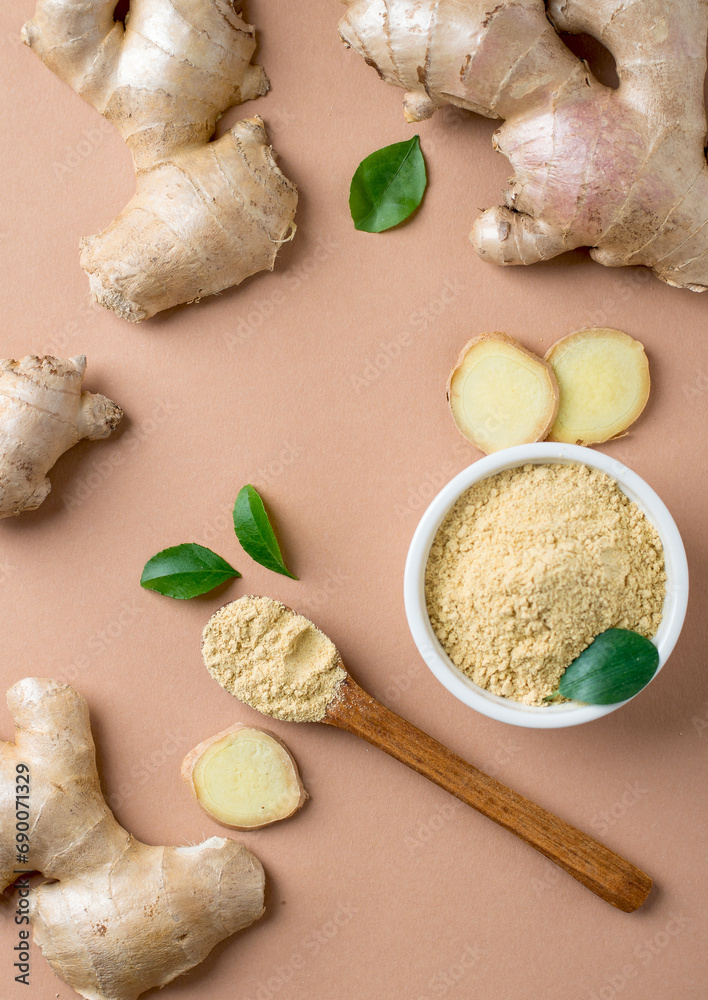 Fototapeta premium Whole, raw ginger, sliced ​​and spice in a bowl and spoon and green leaves on a beige, brown background.