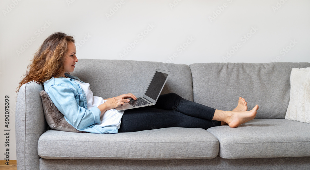 Young brunette woman wearing casual clothes lying down on couch at home and using her laptop. Online shopping, electronic banking, e-commerce. Young brunette woman wearing casual clothes lying down on couch at home and using her laptop. Online shopping, electronic banking, e-commerce.