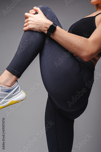 Cropped view of sporty woman in stylish sportswear stretching legs isolated on grey. Healthy and fitness concept