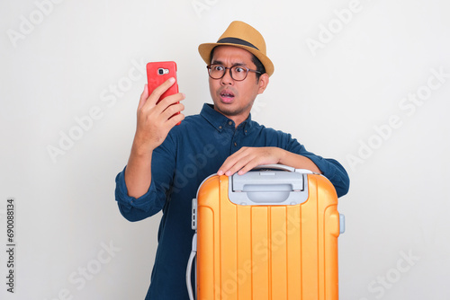 A tourist with luggage looking to his phone with shock expression photo