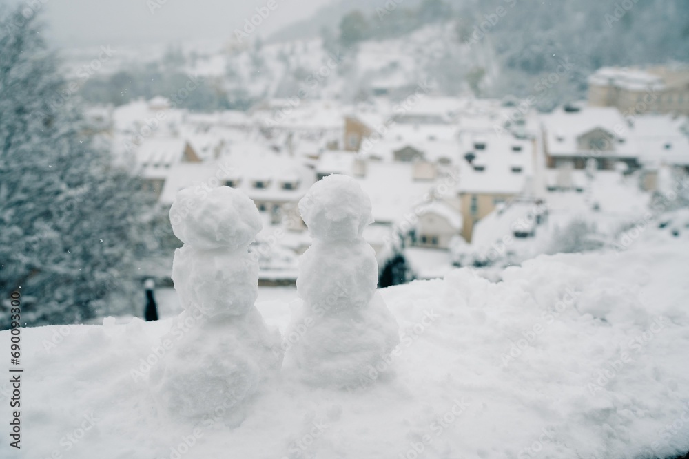Two snowmen on a background of snowy roofs in Prague Two snowmen on a background of snowy roofs in Prague