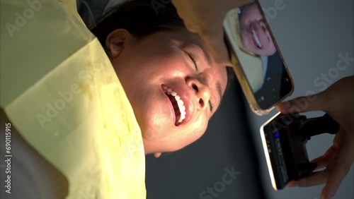 Slow motion vertical shot of a person dentist taking a picture of a latin woman lying down with her mouth open photo