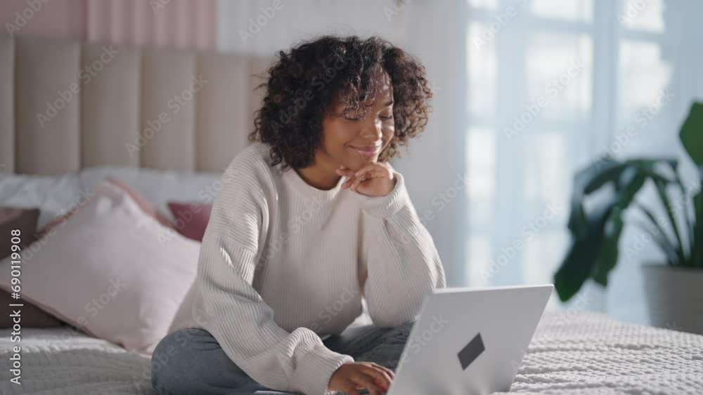 Contented african american woman reading typing messages on laptop chatting with friends sitting in bed at home. Smiling positive curly relaxed female enjoying online communication on computer. Contented african american woman reading typing messages on laptop chatting with friends sitting in bed at home. Smiling positive curly relaxed female enjoying online communication on computer.