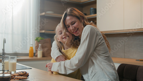 Mother and little daughter cuddle hold hands dancing sitting at table in kitchen breakfast loving mom dance with child girl hugging embracing kid enjoy tender family bonding cuddling. Happy motherhood photo