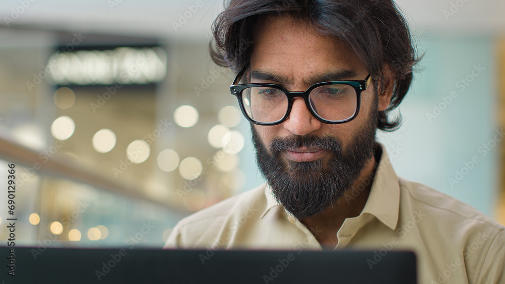 Indian man in glasses looking at laptop screen working online indoors smiling to camera. Close up Arabian businessman worker CEO in eyeglasses work with computer executive entrepreneur looking posing Indian man in glasses looking at laptop screen working online indoors smiling to camera. Close up Arabian businessman worker CEO in eyeglasses work with computer executive entrepreneur looking posing