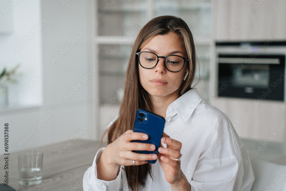 Thoughtful girl in glasses holds phone unhappy reading message at home. Depressed young woman fells loneliness, fatigue concept. Thoughtful girl in glasses holds phone unhappy reading message at home. Depressed young woman fells loneliness, fatigue concept.
