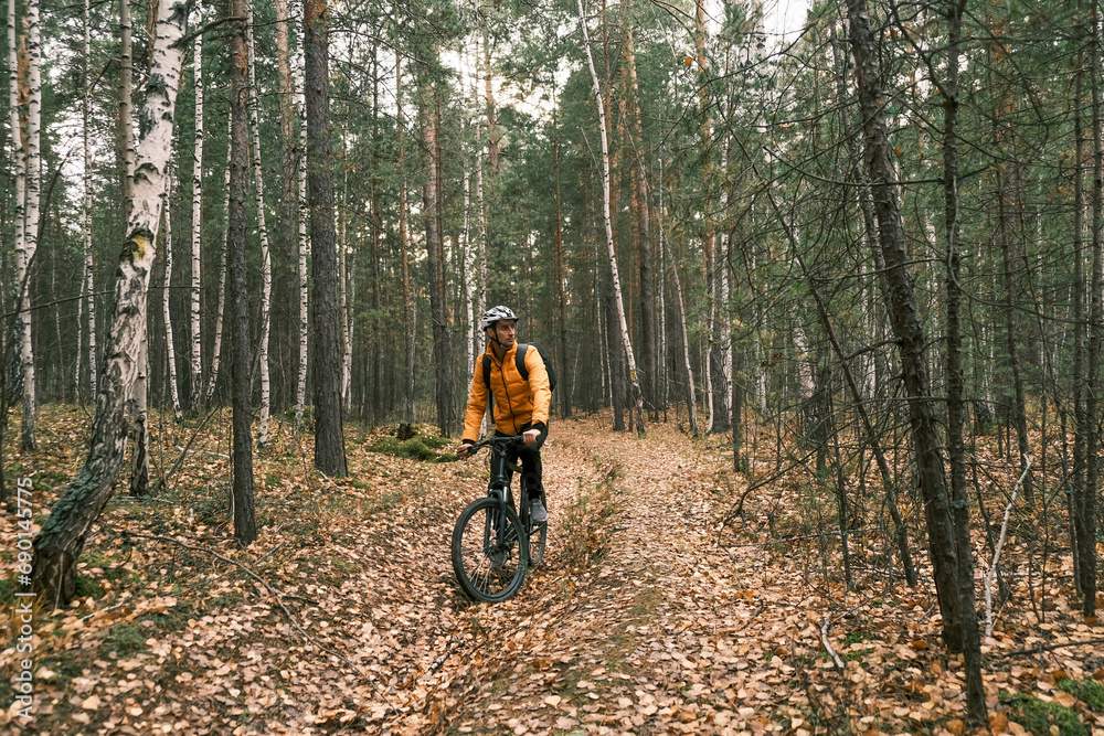 a male cyclist in a protective helmet with a backpack rides a mountain bike through the autumn forest
