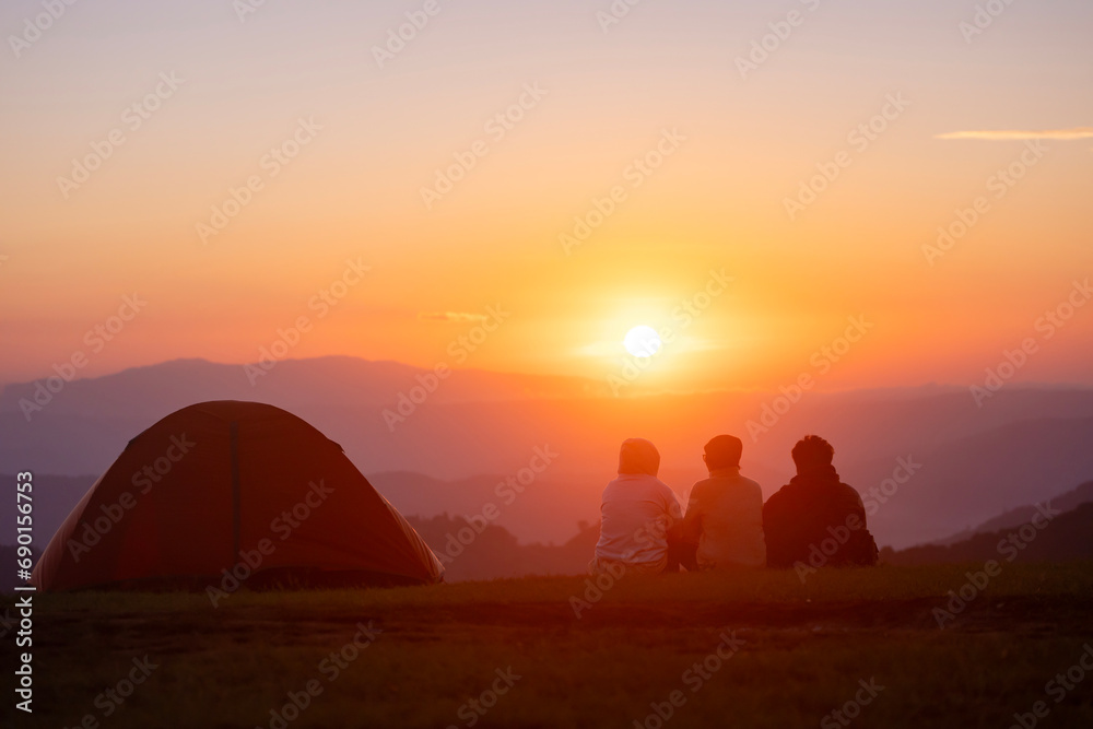 Group of friends sitting by the tent during overnight camping while looking at the beautiful view point sunset over the mountain for outdoor adventure vacation travel