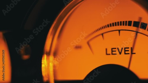 Analog dial indicator of audio signal level. Vintage arrow moves in sync with sound level. Round classic volume indicator with yellow backlight, VU meters. Close-up of old gauge measuring dB decibels photo