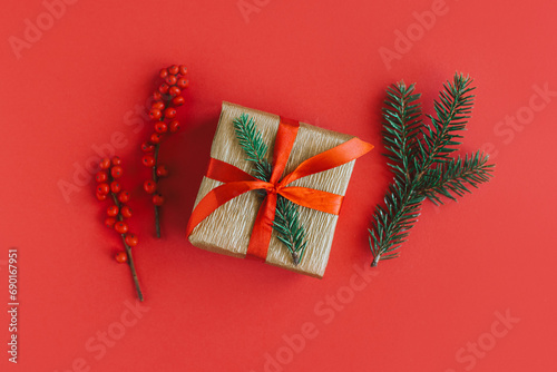 Gift box with spruce branches and red berries on a red background. Holiday concept.