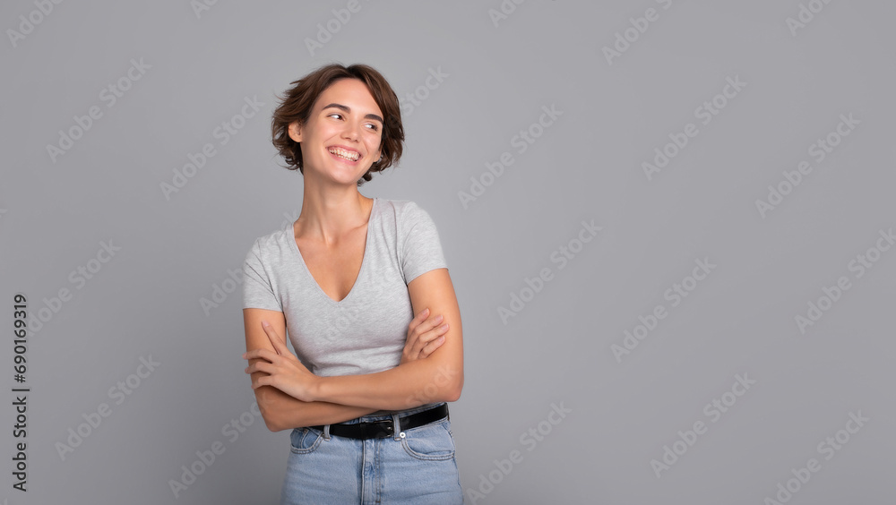Close up photo of beautiful smiling happy young girl with short hair and crossed arms, in casual wear, looking away. Studio shot of cute woman isolated against blank gray wall. Close up photo of beautiful smiling happy young girl with short hair and crossed arms, in casual wear, looking away. Studio shot of cute woman isolated against blank gray wall.