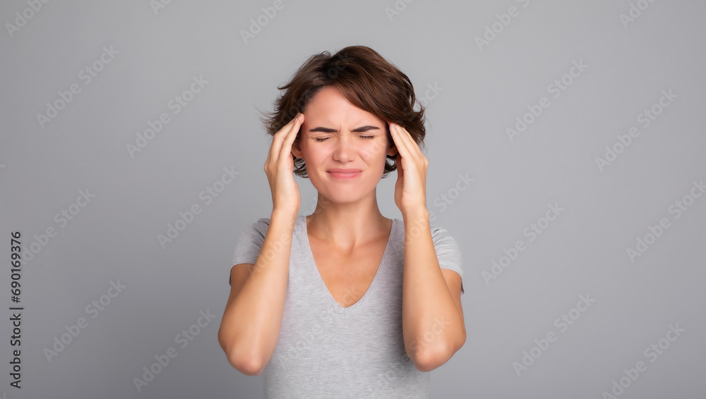 Close up photo of young woman feeling headache, migraine or being ill with short hair in t-shirt touching her head with pain isolated over gray background. Depressed and overworked Close up photo of young woman feeling headache, migraine or being ill with short hair in t-shirt touching her head with pain isolated over gray background. Depressed and overworked