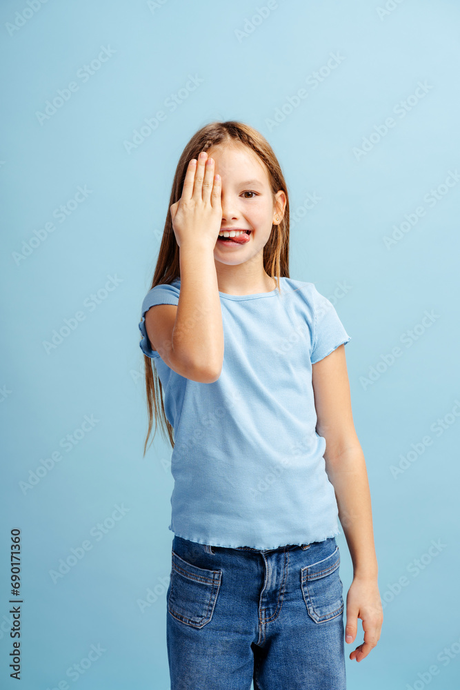 Portrait of smiling beautiful little girl showing tongue, covering eye with hand, fooling around Portrait of smiling beautiful little girl showing tongue, covering eye with hand, fooling around