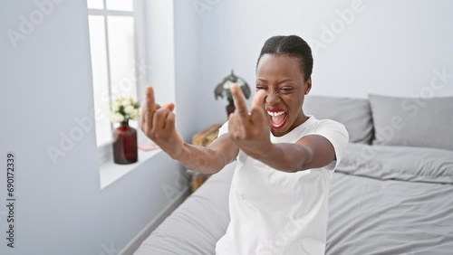 African american woman throws a 'fuck you' middle finger gesture in her bedroom. showing a bad attitude and provocation, she's lying on the bed expressing rude behaviour!