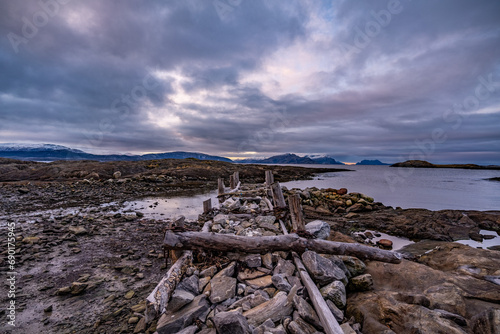 Obraz na płótnie old wooden stone pier during tide on shore of bodo in norway with mountains on background w salonie