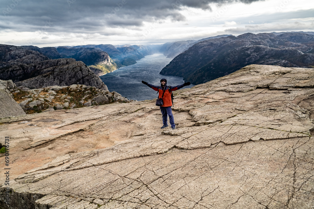 man hiker stands on pulpit rock Preikestolen with Lysefjorden on background during bad weather