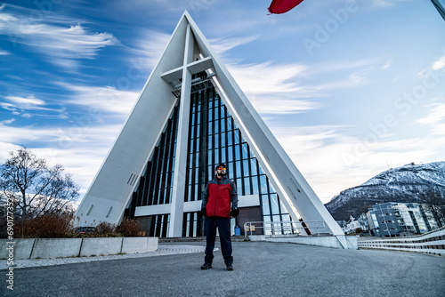 young man with beard stands in front of arctic cathedral in tromso, norway